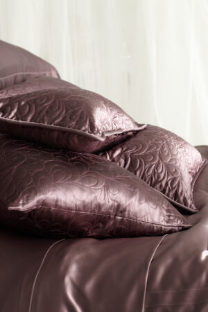 A stack of luxurious plum quilted silk pillows on a matching silk duvet, enhancing the bedroom's opulence.