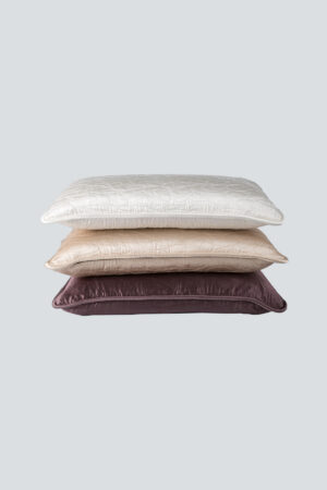 A stack of quilted lumbar silk pillows in varying shades, showcasing the MANITO brand embroidery.