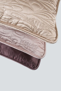 Close-up of embroidered silk pillows with 'MANITO' brand stitching, showcasing the intricate details and plush texture.