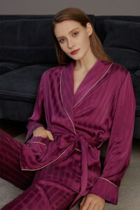 A woman sitting on a carpet next to a sofa wearing MANITO Embossed purple pajama set.