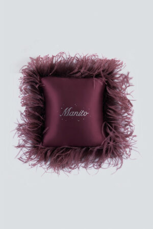 Red holiday throw cushion with decorative feathers and a sparkling rhinestone logo for festive home decor.