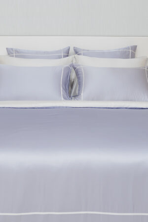 MANITO Fluora Silk Pillowcase Set on a made-up bed, featuring layered color contrasts in lavender and white.