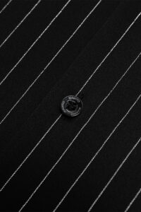 Close-up of black button with MANITO branding on striped silk fabric.