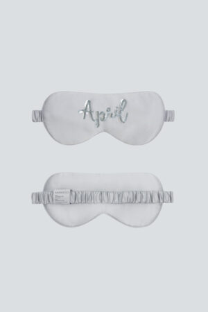 Silver-gray Lune Silk Eye Mask with “April” sequin embroidery and silk-covered strap.