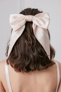 Close-up view of a woman's back of the head, featuring a luxurious silk bow barrette in soft ivory, elegantly embellished with pearls, adding a touch of sophistication.