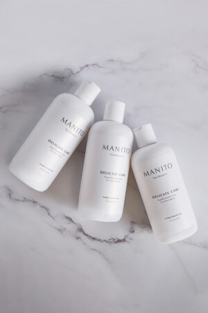 Three MANITO Delicate Care Delicate Laundry Liquid Soap bottles arranged on a marble surface in soft light.
