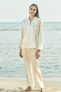 Full-body view of a model in a MANITO rainbow striped long sleeve shirt and pants, standing on the beach.