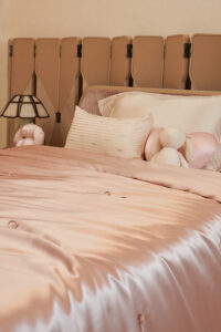 Silk Throw Blanket in blush pink displayed on a neatly made bed with pillows and plush toys.