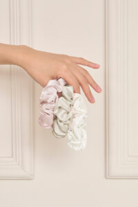 Hand displaying the Sweet Garden Silk Hair Scrunchies Set-Three in three soft floral-inspired shades.