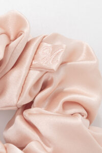 Close-up of pink Thick Silk Scrunchie with embroidered tag, highlighting smooth silk texture.