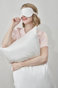 Woman holding white pillow for couples from MANITO Wedding Mr. & Mrs. Silk Pillowcases Gift Box with visible "Mr" embroidery.
