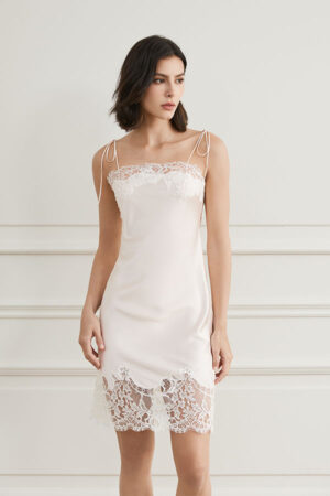 A woman in a Windy Silk White Lace Short Dress, standing against a white paneled wall.