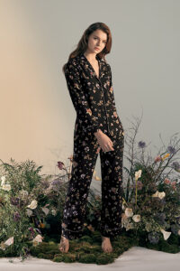 Model posing in a Lrisette Silk Pajama Set with a black floral pattern in a garden setting.