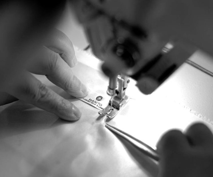 Close-up of a seamstress sewing a MANITO label, showcasing precision in silk garment crafting.