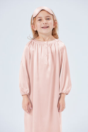 Smiling young girl in a pink silk nightgown with a matching sleep mask.